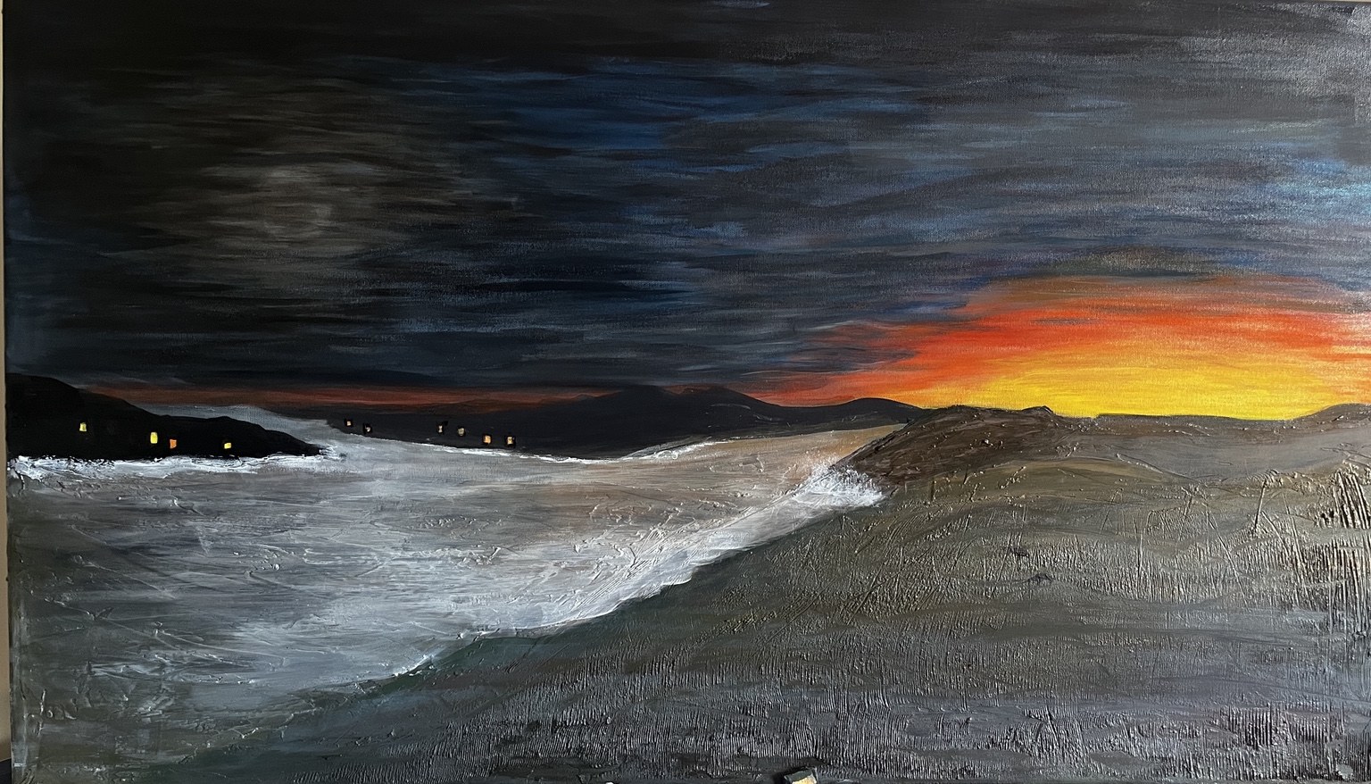A dark coastal sunset with white surf and a narrow orange glow on the horizon